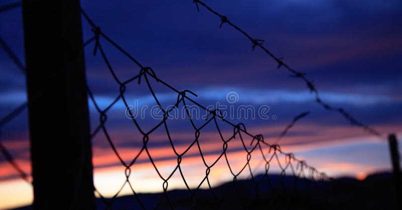 De omheining van het draadnetwerk op silhouetten van polen op de achtergrond van het hemelonduidelijke beeld bij zonsondergang royalty-vrije stock foto's De omheining van het draadnetwerk op silhouetten van polen op de achtergrond van het hemelonduidelijke beeld bij zonsondergang royalty-vrije stock foto's