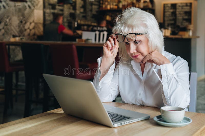 De onderneemster zit bij lijst voor laptop en bekijkt dicht monitor, die haar glazen opheffen Onderwijs voor volwassenen