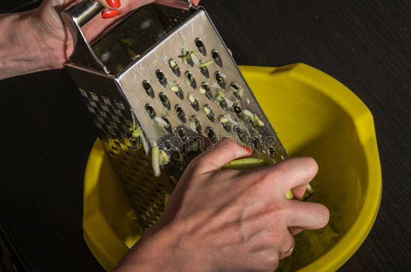 De oneffenheden van de vrouwenkok op raspcourgette stock afbeeldingen De oneffenheden van de vrouwenkok op raspcourgette stock afbeeldingen