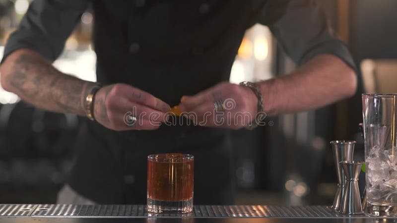 De onherkenbare barman drukt oranje schil in een glas met een cocktail, dan zet de rest in glas dichte omhooggaand