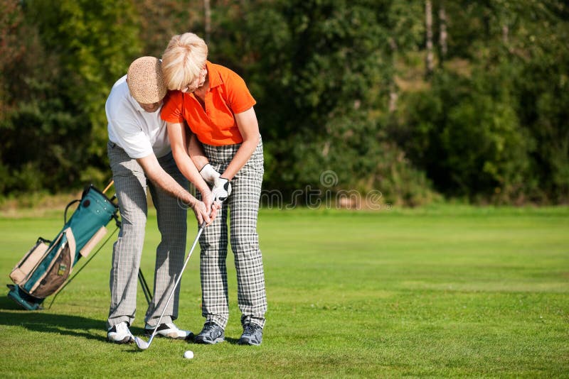 Senior couple playing golf on a summer afternoon, the mal partner is trainer to the female golfer. Senior couple playing golf on a summer afternoon, the mal partner is trainer to the female golfer