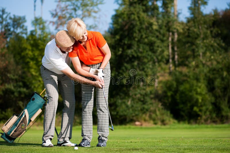 Senior couple playing golf on a summer afternoon, the mal partner is trainer to the female golfer. Senior couple playing golf on a summer afternoon, the mal partner is trainer to the female golfer