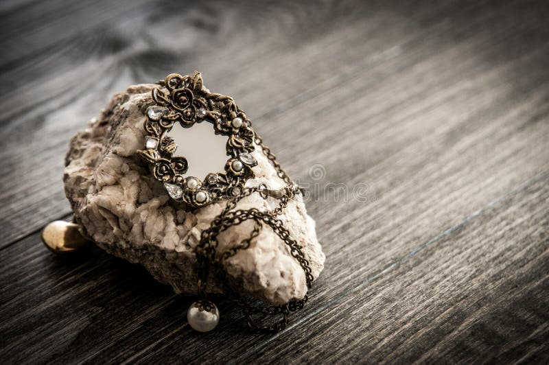 De oude uitstekende ovale spiegelhalsband op een steenmanier heeft op houten lijst bezwaar Gefiltreerd gestemd beeld, royalty-vrije stock afbeelding De oude uitstekende ovale spiegelhalsband op een steenmanier heeft op houten lijst bezwaar Gefiltreerd gestemd beeld, royalty-vrije stock afbeelding
