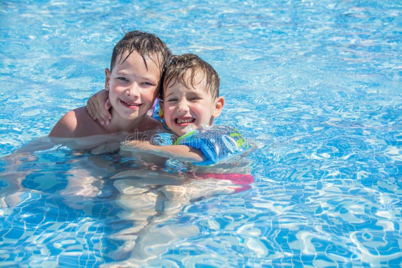 De oudere broer en de jongere broer zwemmen in de pool van de openluchtkinderen stock afbeelding De oudere broer en de jongere broer zwemmen in de pool van de openluchtkinderen stock afbeelding
