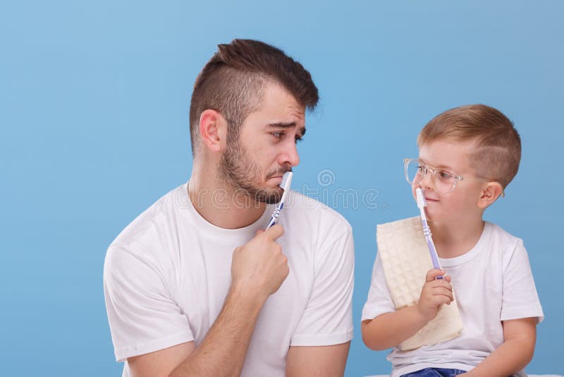 De papa en zijn zoon zetten borstels aan hun lippen en bekijken elkaar tegen een blauwe achtergrond royalty-vrije stock foto De papa en zijn zoon zetten borstels aan hun lippen en bekijken elkaar tegen een blauwe achtergrond royalty-vrije stock foto