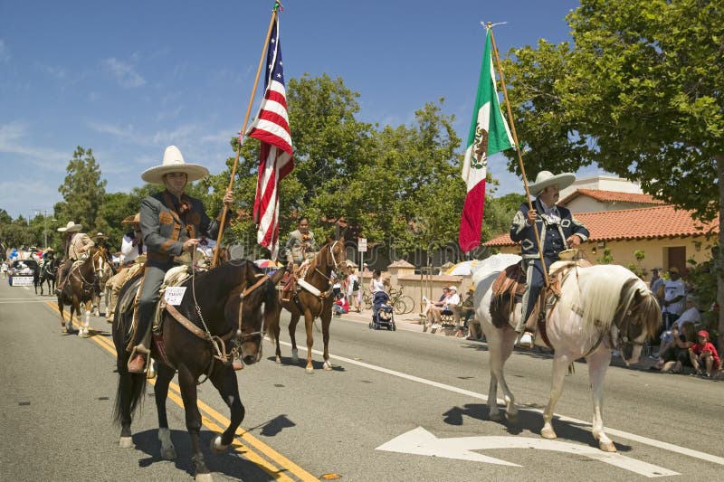 De paradedeelnemers op horseback die Amerikaanse en Mexicaanse vlaggen dragen maken hun manier onderaan hoofdstraat tijdens een V stock fotografie De paradedeelnemers op horseback die Amerikaanse en Mexicaanse vlaggen dragen maken hun manier onderaan hoofdstraat tijdens een V stock fotografie