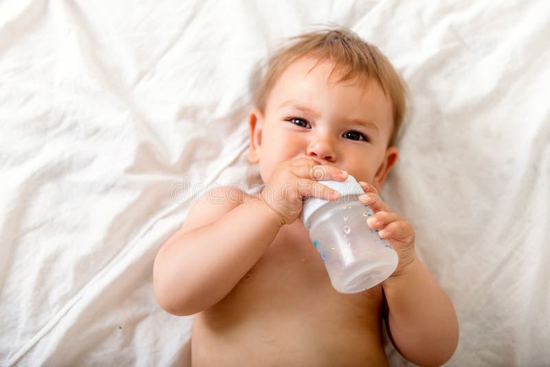 De peuterbaby drinkt water van blauwe plastic fles het zitten op witte achtergrond De ruimte van het exemplaar stock foto De peuterbaby drinkt water van blauwe plastic fles het zitten op witte achtergrond De ruimte van het exemplaar stock foto