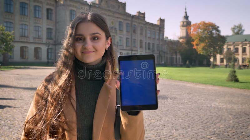 De plezierige Kaukasische vrouw bevindt zich en toont het blauwe scherm met gelukkige glimlach en toevallige de rust ziet eruit