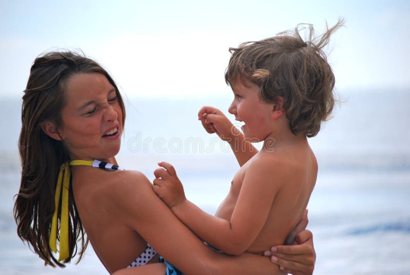 A sister holding her brother or girl and boy having fun on the beach and showing expressions on their faces of fun and love and nose scrunching. A sister holding her brother or girl and boy having fun on the beach and showing expressions on their faces of fun and love and nose scrunching.
