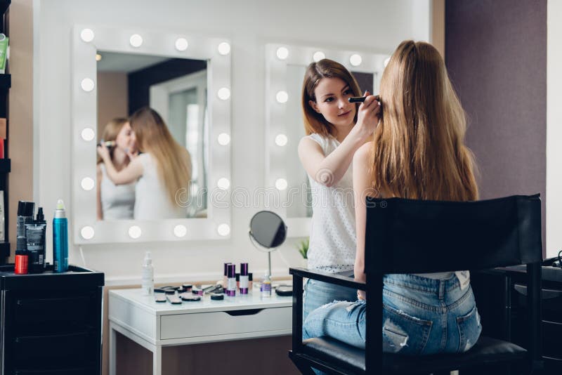 De professionele make-upkunstenaar die bij het jonge meisje natuurlijk creëren werken kijkt in schoonheidssalon