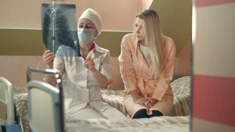 De professionele röntgenstraal van de artsenholding en het spreken aan jonge vrouwelijke geduldige zitting op bed royalty-vrije stock foto's De professionele röntgenstraal van de artsenholding en het spreken aan jonge vrouwelijke geduldige zitting op bed royalty-vrije stock foto's