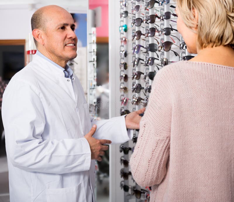 de rijpe cliënt die van de mensenopticien Rijp Blonde adviseren dichtbij de vertoningszonnebril stock fotografie de rijpe cliënt die van de mensenopticien Rijp Blonde adviseren dichtbij de vertoningszonnebril stock fotografie