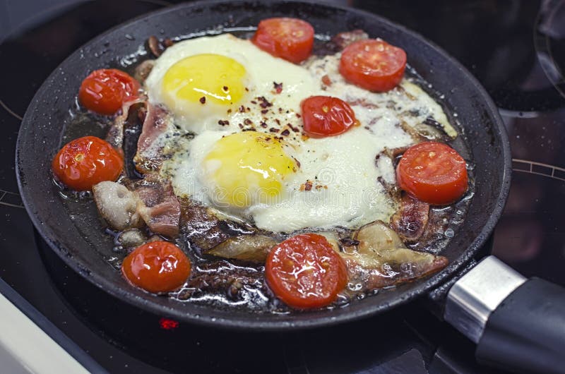 De roereieren die in een pan koken, die op een ceramisch fornuis koken, braadden eieren met bacon en tomaat, 45 meningsclose-up stock fotografie De roereieren die in een pan koken, die op een ceramisch fornuis koken, braadden eieren met bacon en tomaat, 45 meningsclose-up stock fotografie