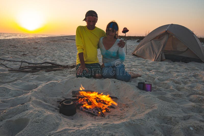 De romantische reizigers zitten naast een brandende brand op het strand royalty-vrije stock afbeelding De romantische reizigers zitten naast een brandende brand op het strand royalty-vrije stock afbeelding