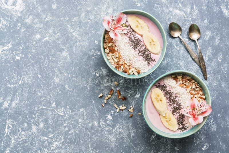 De roze yoghurt met amandelen, banaan, chiazaden en kokosnoot schilfert in blauwe kommen op een grijze die achtergrond af met blo royalty-vrije stock afbeeldingen De roze yoghurt met amandelen, banaan, chiazaden en kokosnoot schilfert in blauwe kommen op een grijze die achtergrond af met blo royalty-vrije stock afbeeldingen