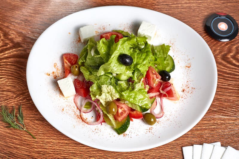 De salade met mozarellakaas van komkommers, tomaten, olijven, groene paprika's, uiringen, sla, ligt op een witte plaat stock afbeelding De salade met mozarellakaas van komkommers, tomaten, olijven, groene paprika's, uiringen, sla, ligt op een witte plaat stock afbeelding