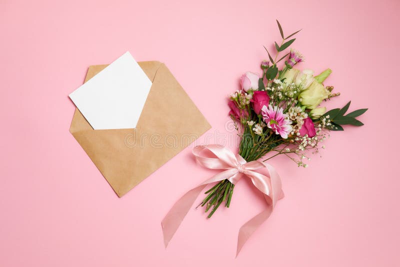 De samenstelling van de valentijnskaartendag: het boeket van bloemen, kraftpapier-envelop met groetkaart legt bij roze achtergron