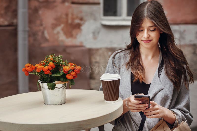De schitterende jonge telefoon van de vrouwenholding, en kop van koffie en zak stock afbeelding De schitterende jonge telefoon van de vrouwenholding, en kop van koffie en zak stock afbeelding