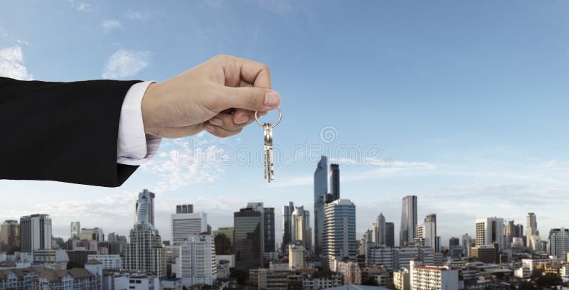 De sleutels van de handholding met de stadsachtergrond van Bangkok, het kopen onroerende goederen huis, en huishuurconcepten stock fotografie De sleutels van de handholding met de stadsachtergrond van Bangkok, het kopen onroerende goederen huis, en huishuurconcepten stock fotografie