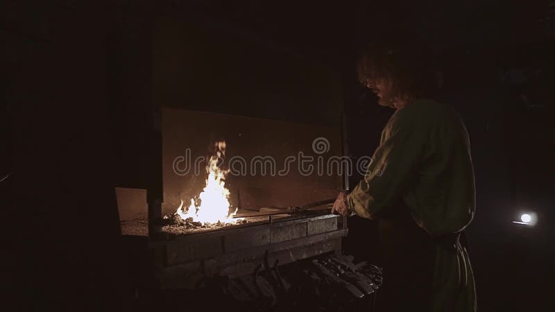 De smid houdt het werkstuk op de steenkolen in smeedt oven verwarmend het vóór smeedstuk Hij is bezig geweest met de vervaardigin