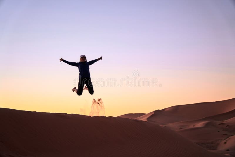 De sprongen van het toeristenmeisje bij het woestijnduin tijdens zonsondergang royalty-vrije stock foto De sprongen van het toeristenmeisje bij het woestijnduin tijdens zonsondergang royalty-vrije stock foto