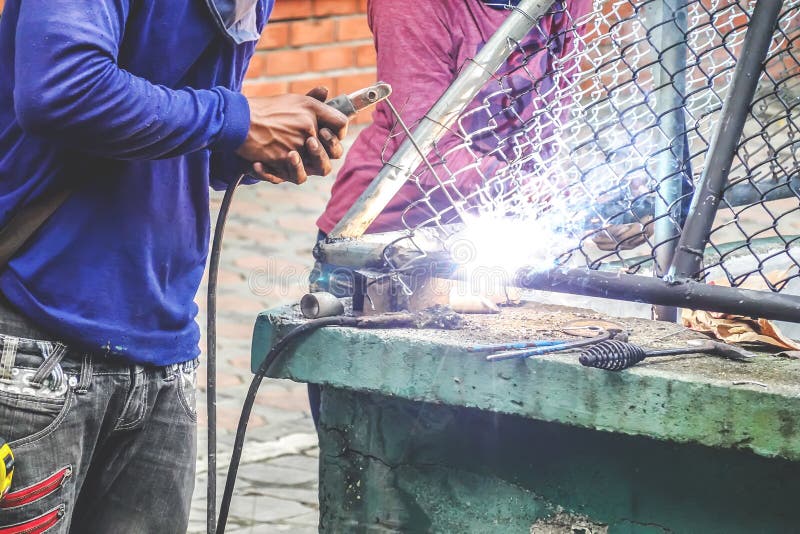 De sterke mens is een lasser in een blauwe T-shirt, en het lassersleer, een metaalproduct is gelast met een lassenmachine in open royalty-vrije stock fotografie De sterke mens is een lasser in een blauwe T-shirt, en het lassersleer, een metaalproduct is gelast met een lassenmachine in open royalty-vrije stock fotografie