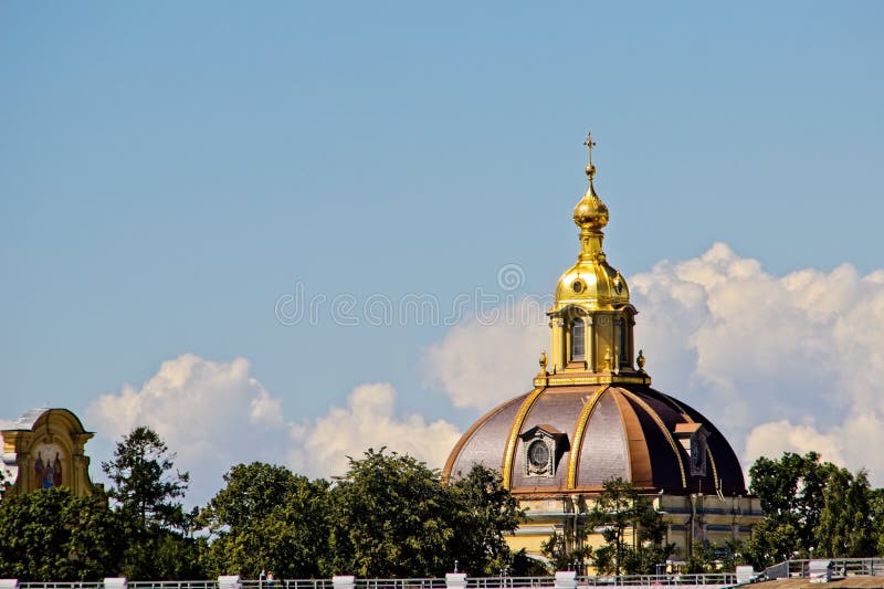 View of the magnificent dome of the chapel of the Grand Duke's tomb, gilded decorations in the Baroque style, dome and Orthodox cross, details and elements of architecture, city attractions, green plants, sky and clouds, cityscape, travel and tourism, summer. View of the magnificent dome of the chapel of the Grand Duke's tomb, gilded decorations in the Baroque style, dome and Orthodox cross, details and elements of architecture, city attractions, green plants, sky and clouds, cityscape, travel and tourism, summer.