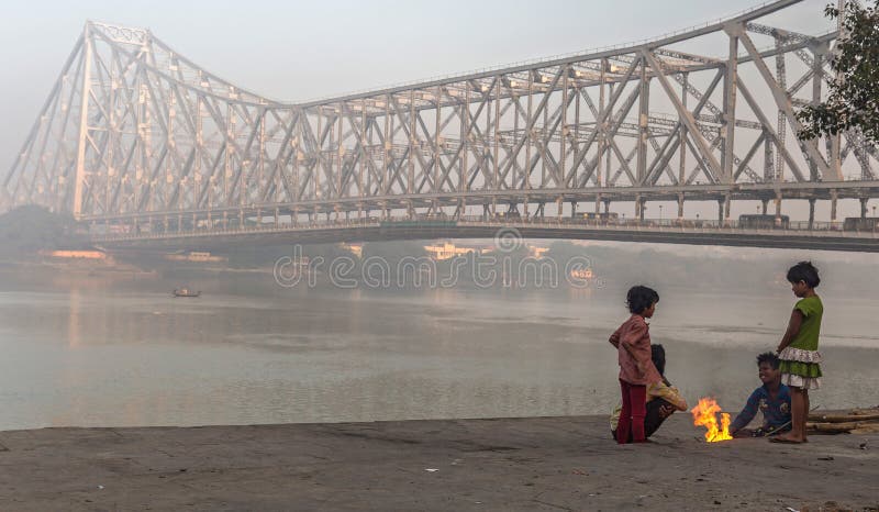 De straatjonge geitjes houden op een koude mistige de winterochtend warm in Mallick ghat dichtbij de brug van Howrah bij de bank royalty-vrije stock foto De straatjonge geitjes houden op een koude mistige de winterochtend warm in Mallick ghat dichtbij de brug van Howrah bij de bank royalty-vrije stock foto