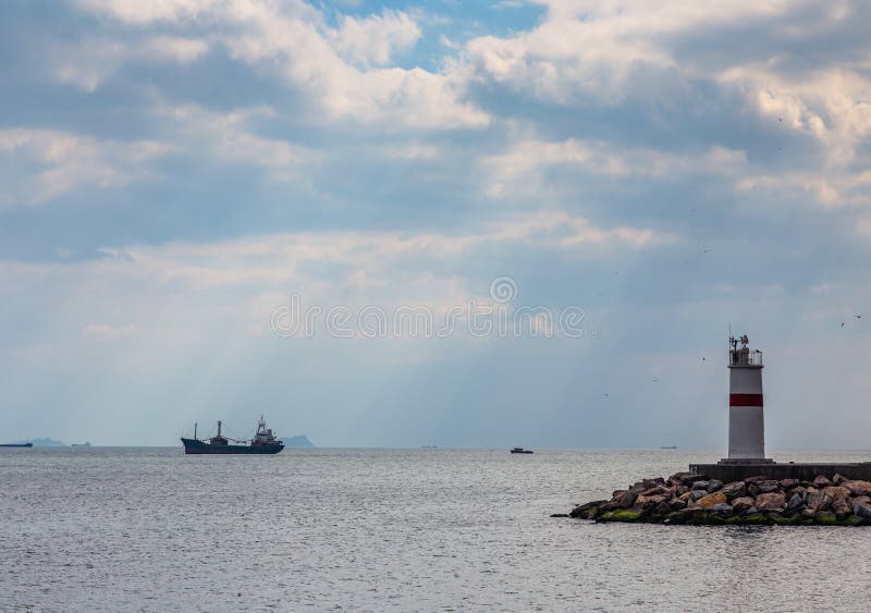 De stralen van de zon verlichten de vuurtoren en het schip in de wegen door de wolken bij de ingang aan Bosphorus, stock fotografie De stralen van de zon verlichten de vuurtoren en het schip in de wegen door de wolken bij de ingang aan Bosphorus, stock fotografie
