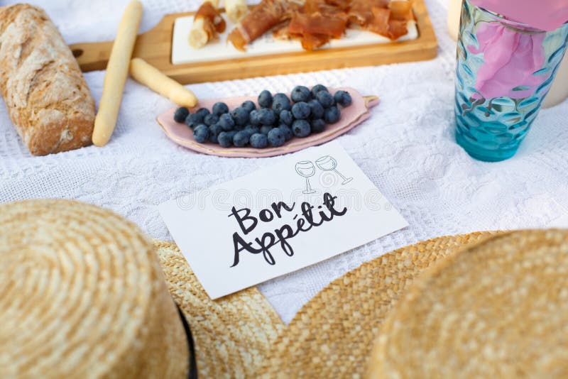 De strohoeden leggen op een witte picknickdeken naast de dagachtergrond van de naambord bon apetit heldere zomer De vrije tijd va royalty-vrije stock afbeeldingen De strohoeden leggen op een witte picknickdeken naast de dagachtergrond van de naambord bon apetit heldere zomer De vrije tijd va royalty-vrije stock afbeeldingen