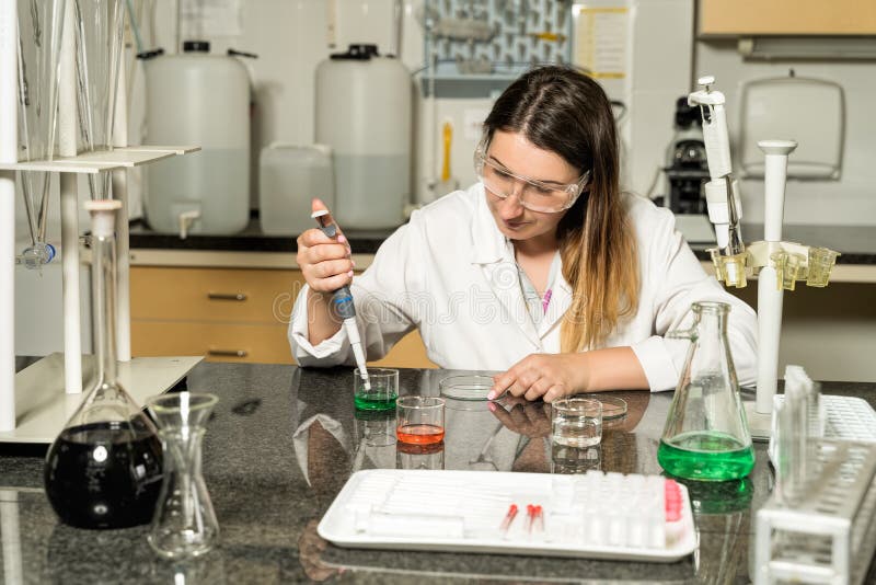 De technicusbemonstering van het middenleeftijds vrouwelijke laboratorium met pipet chemische vloeibare oplossing in laboratorium stock afbeelding De technicusbemonstering van het middenleeftijds vrouwelijke laboratorium met pipet chemische vloeibare oplossing in laboratorium stock afbeelding