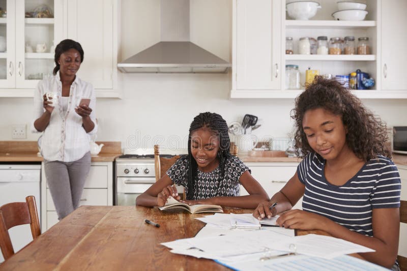 De Telefoon van het moedergebruik als Dochters Sit At Table Doing Homework royalty-vrije stock foto De Telefoon van het moedergebruik als Dochters Sit At Table Doing Homework royalty-vrije stock foto