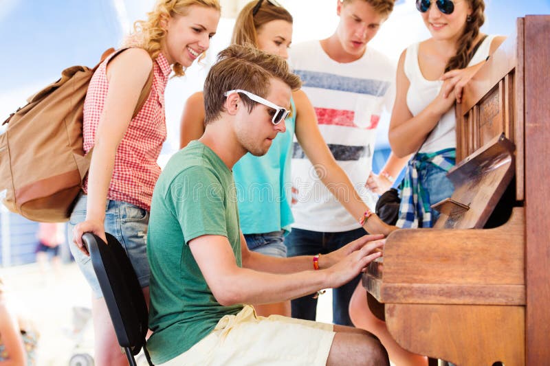 Group of teenage boys and girls at summer music festival, handsome young men plays the piano. Sunny day. Group of teenage boys and girls at summer music festival, handsome young men plays the piano. Sunny day.