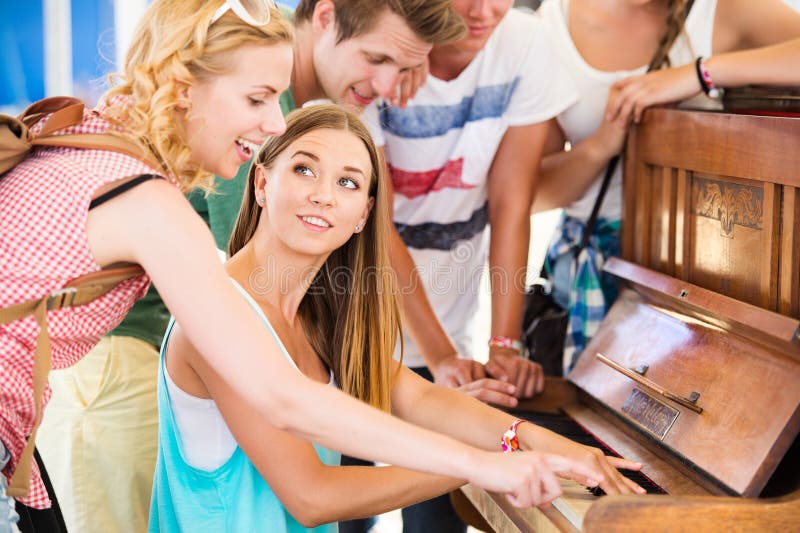 Group of teenage boys and girls at summer music festival, beautiful young women plays the piano. Sunny day. Group of teenage boys and girls at summer music festival, beautiful young women plays the piano. Sunny day.