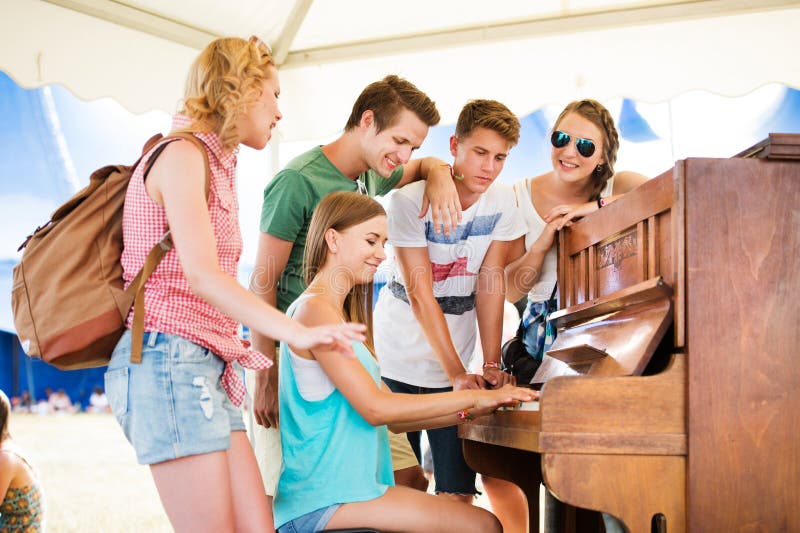 Group of teenage boys and girls at summer music festival, beautiful young women plays the piano. Sunny day. Group of teenage boys and girls at summer music festival, beautiful young women plays the piano. Sunny day.