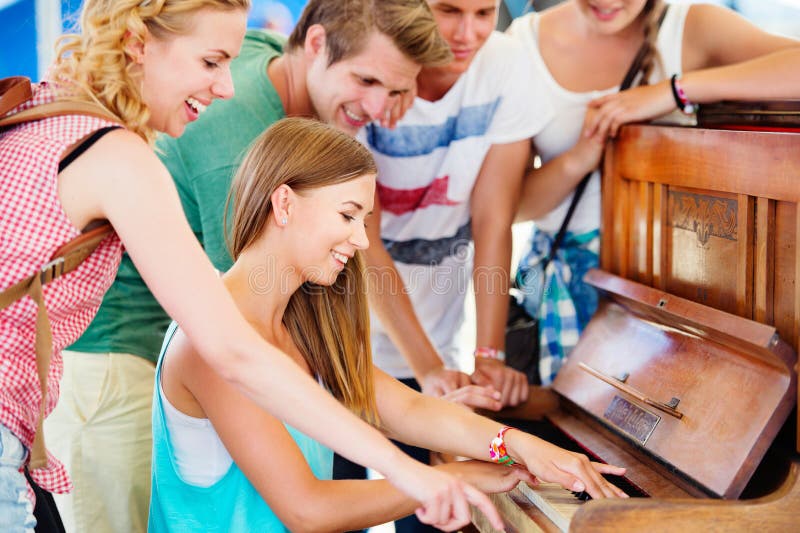 Group of teenage boys and girls at summer music festival, beautiful young women plays the piano. Sunny day. Group of teenage boys and girls at summer music festival, beautiful young women plays the piano. Sunny day.