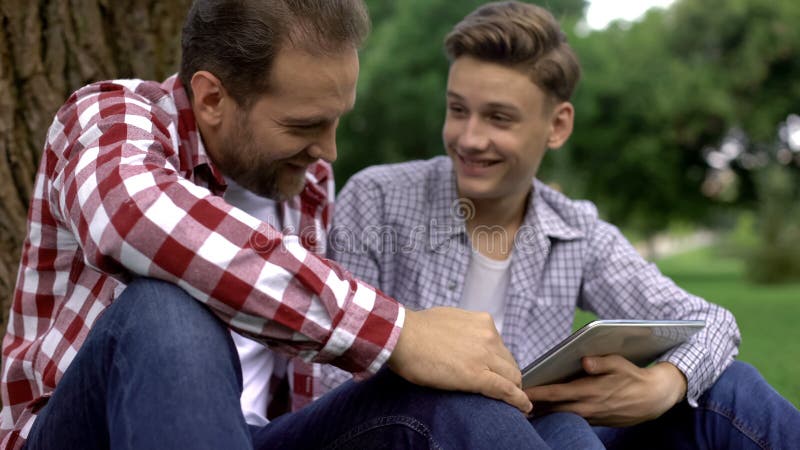 De tienerzoon die foto's van zijn meisje tonen aan vader, mensen spreekt, vertrouwensrelaties stock foto De tienerzoon die foto's van zijn meisje tonen aan vader, mensen spreekt, vertrouwensrelaties stock foto