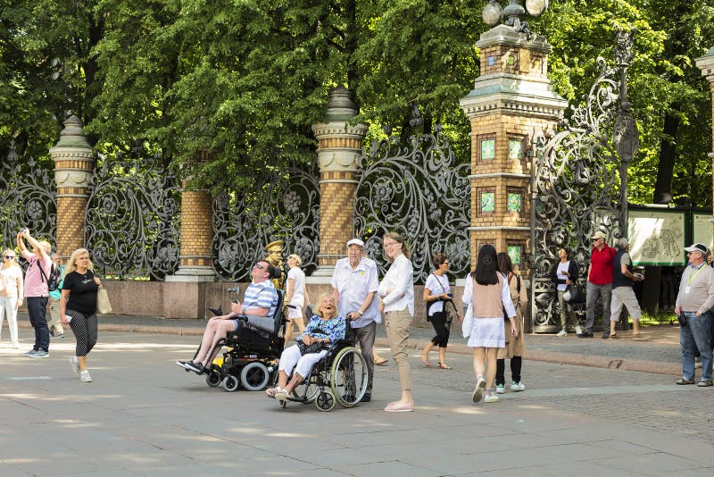 De toeristen in rolstoelen bij de omheining van Mikhailovsky tuinieren bekijken de Kerk van de Verlosser op Bloed Heilige Petersb royalty-vrije stock afbeelding De toeristen in rolstoelen bij de omheining van Mikhailovsky tuinieren bekijken de Kerk van de Verlosser op Bloed Heilige Petersb royalty-vrije stock afbeelding