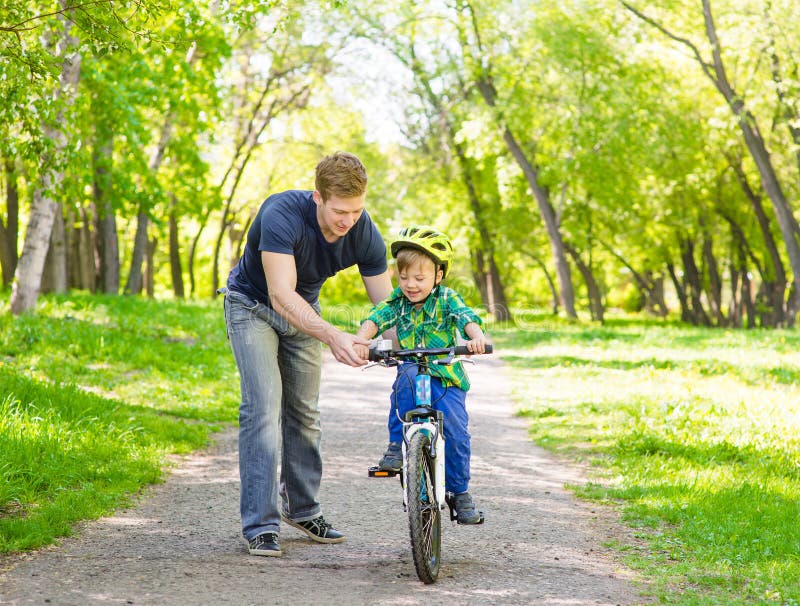 De vader onderwijst zijn zoon om een fiets in park te berijden
