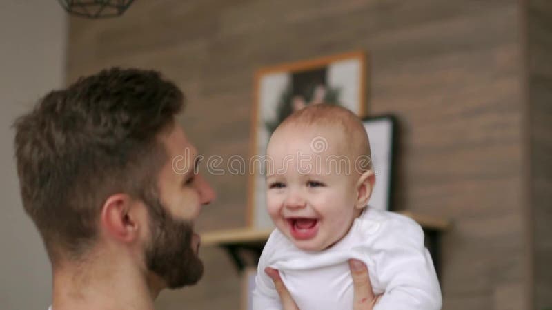 De vaderspelen met zuigelingszoon in witte t-shirt bekijkt hem en lacht Lachende baby die de camera bekijken loving