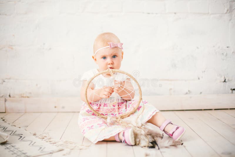 De vanger van de amuletdroom en weinig babymeisje één jaar met blauwe ogen, blonde zitten op de vloer in een kleding en houden royalty-vrije stock fotografie De vanger van de amuletdroom en weinig babymeisje één jaar met blauwe ogen, blonde zitten op de vloer in een kleding en houden royalty-vrije stock fotografie