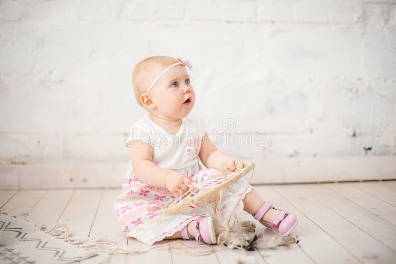 De vanger van de amuletdroom en weinig babymeisje één jaar met blauwe ogen, blonde zitten op de vloer in een kleding en houden royalty-vrije stock fotografie De vanger van de amuletdroom en weinig babymeisje één jaar met blauwe ogen, blonde zitten op de vloer in een kleding en houden royalty-vrije stock fotografie