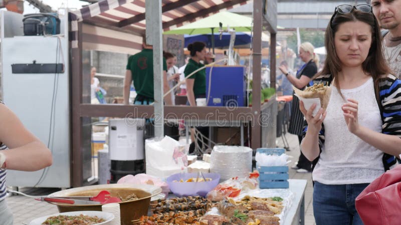 De verkoper geeft koperstroep etend in handen, mensen op voedselmarkt op straat, koopt het wijfje straatmaaltijd in snel voedsel