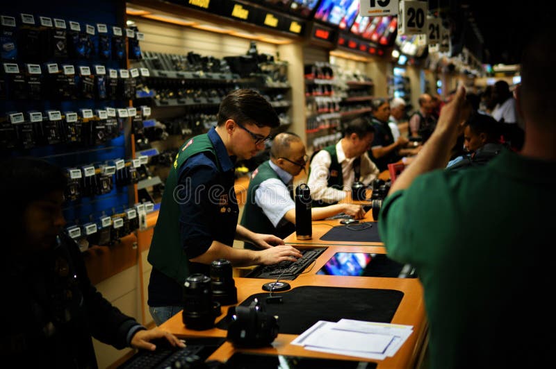 De verkopers zijn achter de teller, typt één verkoper iets op toetsenbord, terwijl de mensen bij de Foto Videoopslag van B&H van stock afbeelding De verkopers zijn achter de teller, typt één verkoper iets op toetsenbord, terwijl de mensen bij de Foto Videoopslag van B&H van stock afbeelding