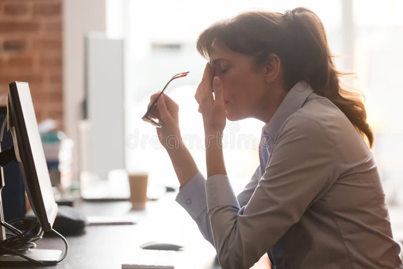 De vermoeide vrouwelijke werknemer lijdt aan hoofdpijn op het werk