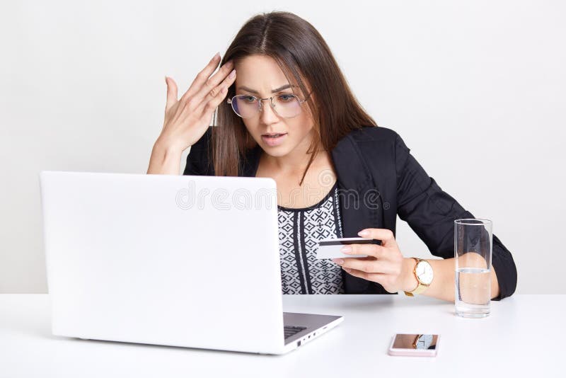 De verraste vrouw met ontevreden uitdrukking, maakt online transactie, werkt met laptop computer, maakt het winkelen in Webopslag stock fotografie De verraste vrouw met ontevreden uitdrukking, maakt online transactie, werkt met laptop computer, maakt het winkelen in Webopslag stock fotografie