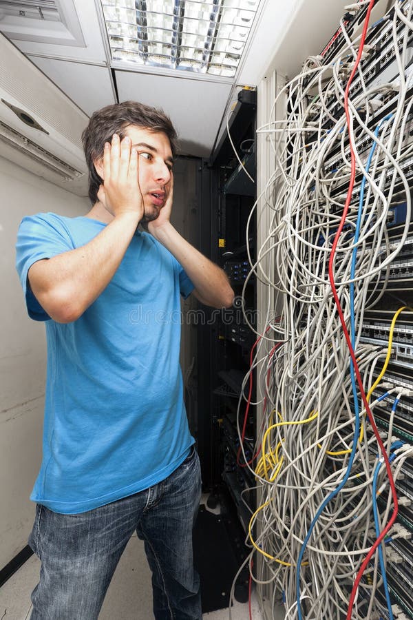 Adult man in his early 30's looking with horror on the tangled cable chaos on the server in front of him. Poor network administrator. Adult man in his early 30's looking with horror on the tangled cable chaos on the server in front of him. Poor network administrator...