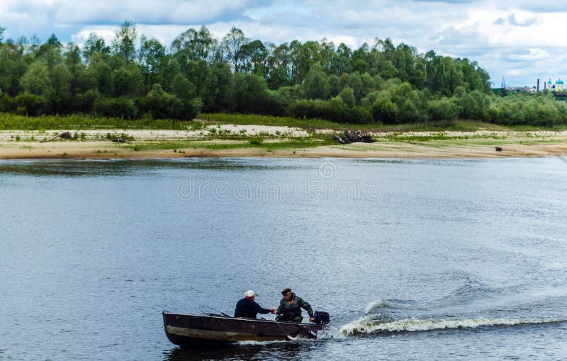 De vissers bewegen zich in een motorboot door het water tegen een achtergrond van groene bomen en een blauwe hemel stock foto De vissers bewegen zich in een motorboot door het water tegen een achtergrond van groene bomen en een blauwe hemel stock foto