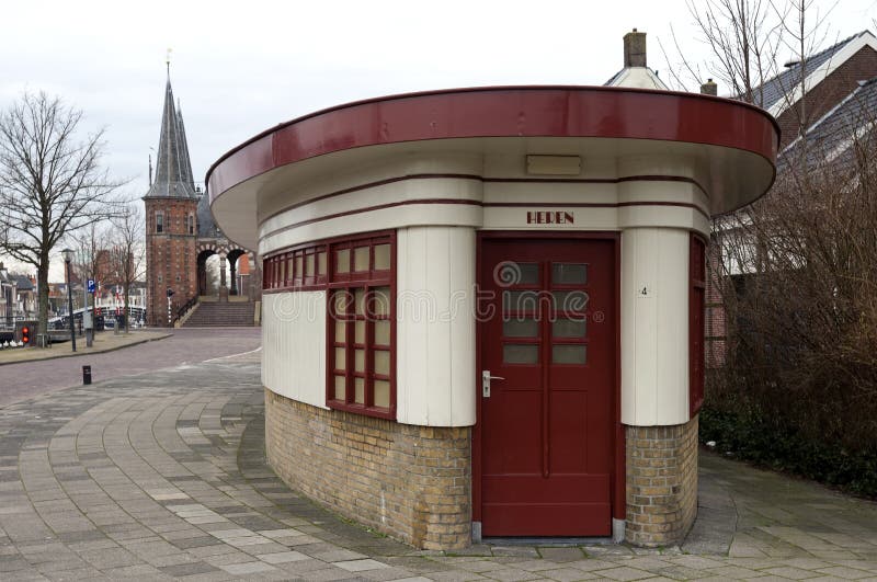 Netherlands province of Friesland, city Sneek [municipality Sudwest Fryslân]: In the foreground the toilet block and shower block for pleasure or recreational boating. This historic building was built as a messenger home building by the city architect, Jan de Kok in 1926 in the Amsterdam School architectural style. Were originally two separate office buildings, but in 1932 they were connected and the building was thereafter elliptical. This building is a municipal monument, landmark, cultural heritage site and tourist attraction. On this side is de room for men [Heren]. Like the ancient structure in the background, the city gate the Waterpoort. Netherlands province of Friesland, city Sneek [municipality Sudwest Fryslân]: In the foreground the toilet block and shower block for pleasure or recreational boating. This historic building was built as a messenger home building by the city architect, Jan de Kok in 1926 in the Amsterdam School architectural style. Were originally two separate office buildings, but in 1932 they were connected and the building was thereafter elliptical. This building is a municipal monument, landmark, cultural heritage site and tourist attraction. On this side is de room for men [Heren]. Like the ancient structure in the background, the city gate the Waterpoort.