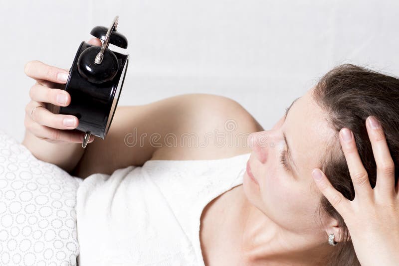 De vrouw bekijkt wekker liggend in bed in ochtend het meisje staat vroeg voor het werk op Sta op de wekker op stock afbeeldingen De vrouw bekijkt wekker liggend in bed in ochtend het meisje staat vroeg voor het werk op Sta op de wekker op stock afbeeldingen